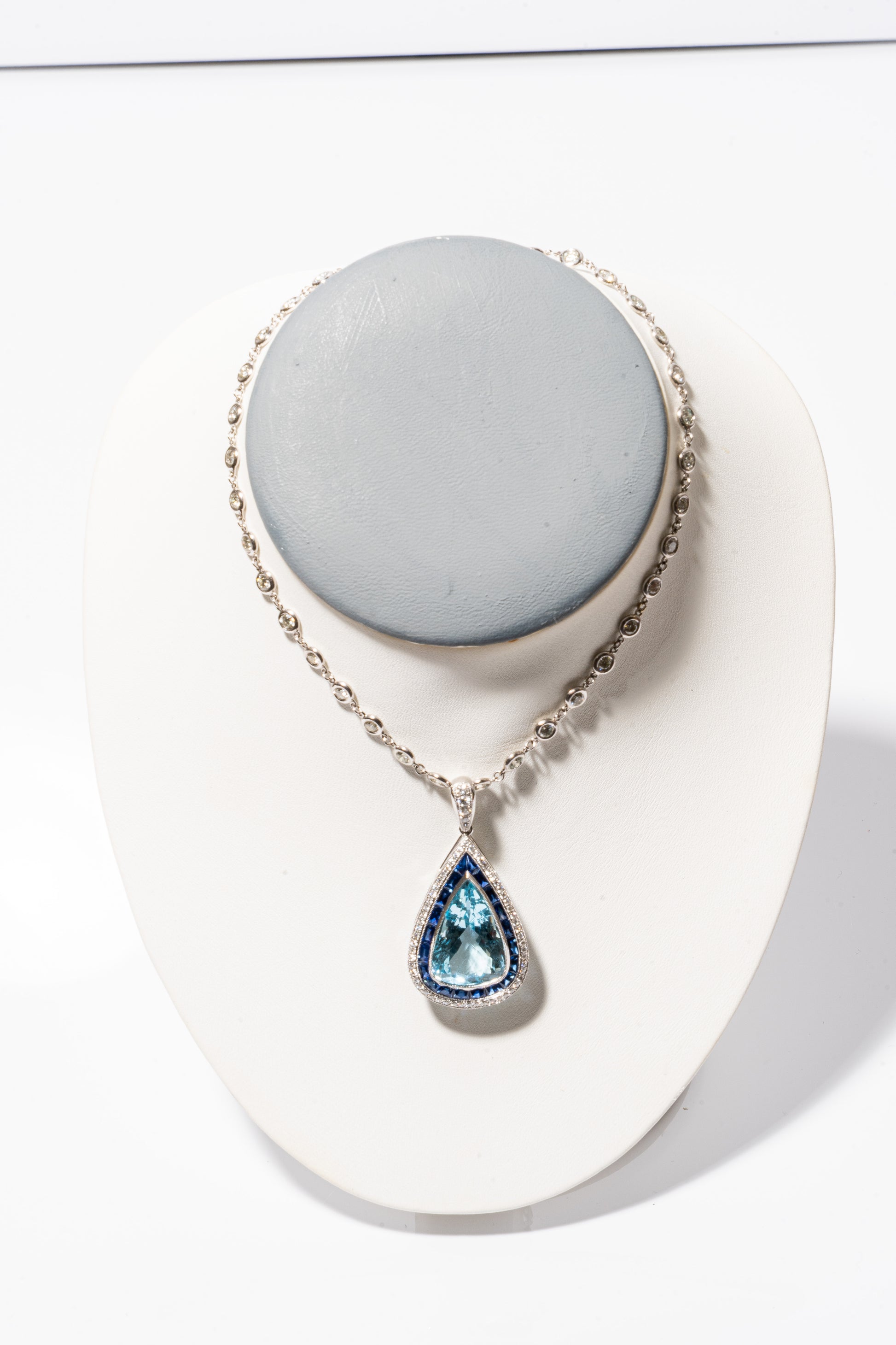 A photo of Pear-Shaped Aquamarine Pendant with sapphires and diamonds on a white gold diamond necklace. 