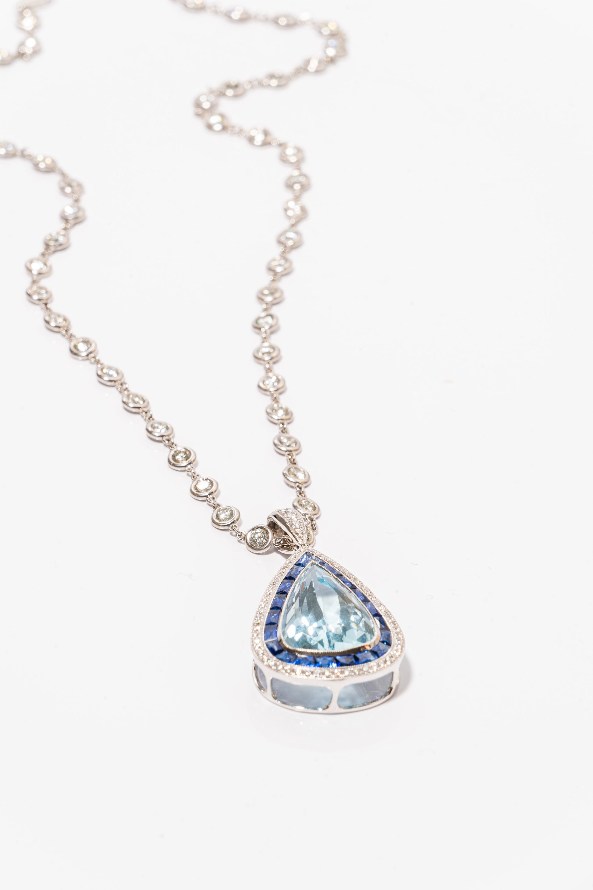 A photo of Pear-Shaped Aquamarine Pendant with sapphires and diamonds on a white gold diamond necklace. 