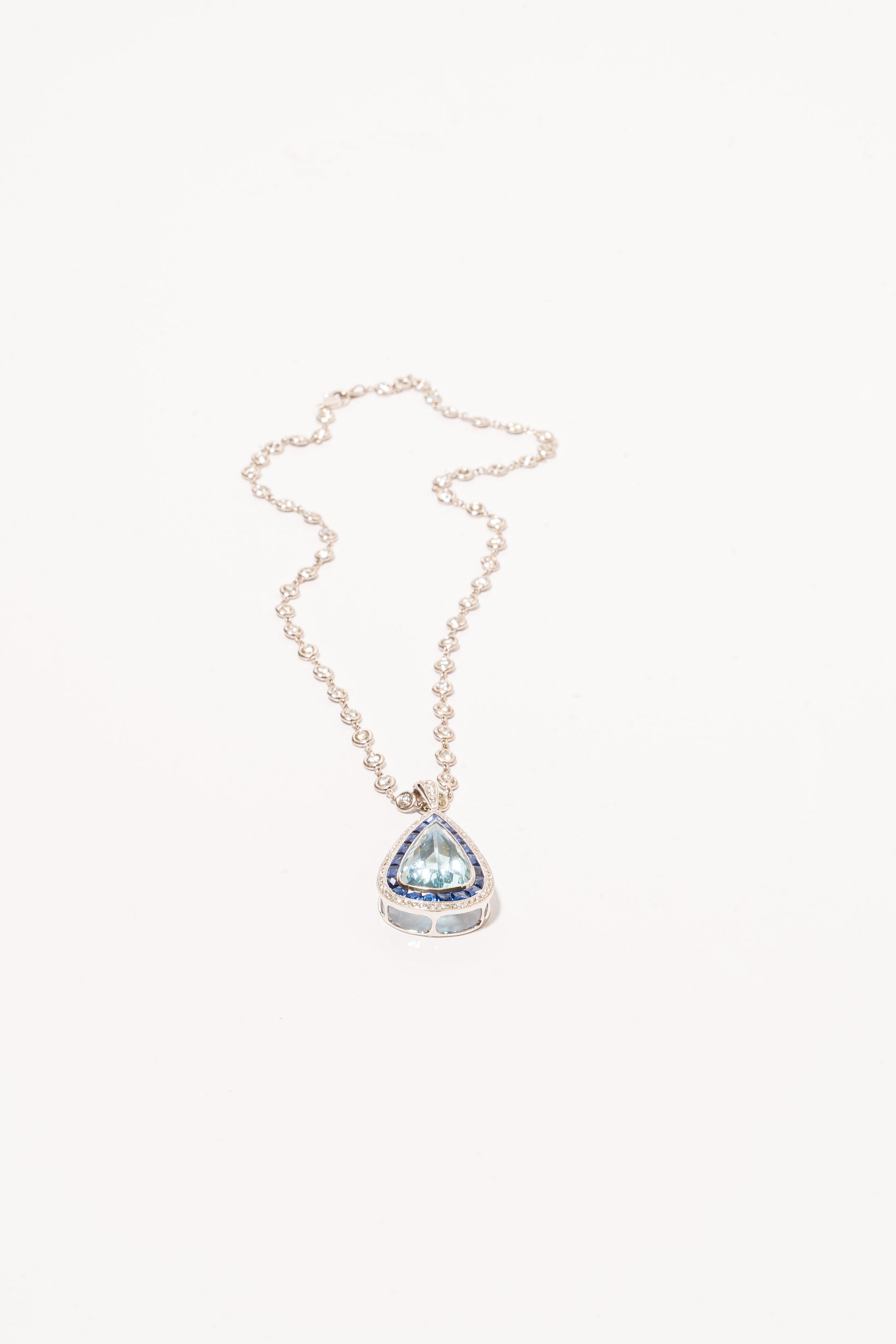 A photo of Pear-Shaped Aquamarine Pendant with sapphires and diamonds on a white gold diamond necklace. 